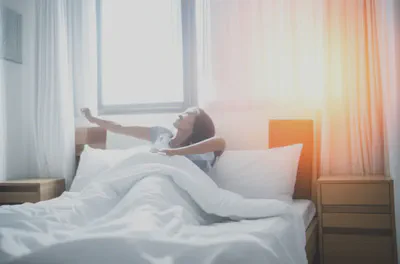 햇살 가득한 방에서 상쾌하게 기지개를 켜는 사람, 불면증 극복 후의 활기찬 아침을 상징