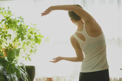 밝은 방에서 스트레칭하는 사람의 뒷모습. 건강한 생활 습관을 상징합니다.